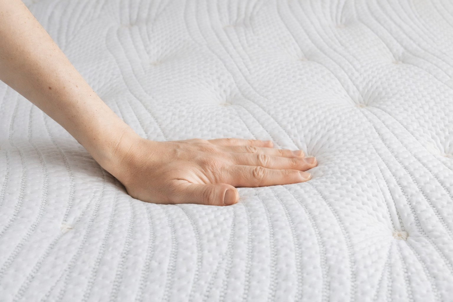 Hand pressing on a Luxe extra firm mattress, showing the supportive feel of the quilted top